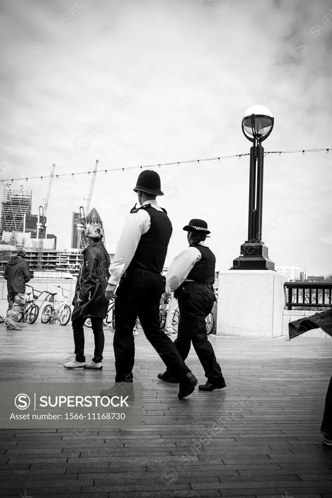 Policeman and policewoman patrol London, near city hall in Thames river path.