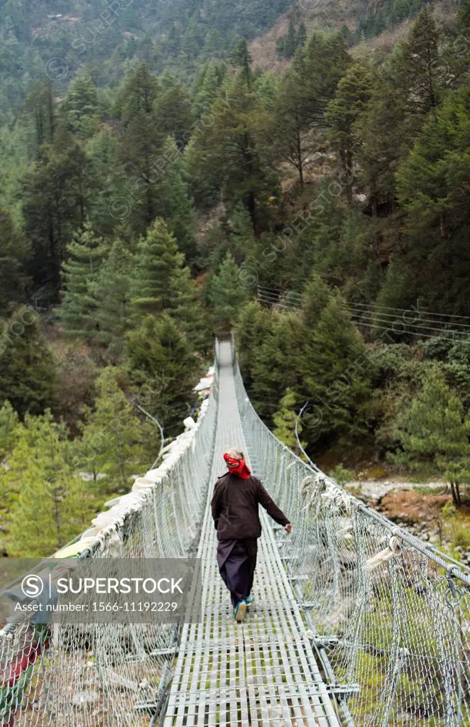 Nepal Himalayas Woman walking across long suspension bridge in Solukhumbu remopte Mt Everest 63.