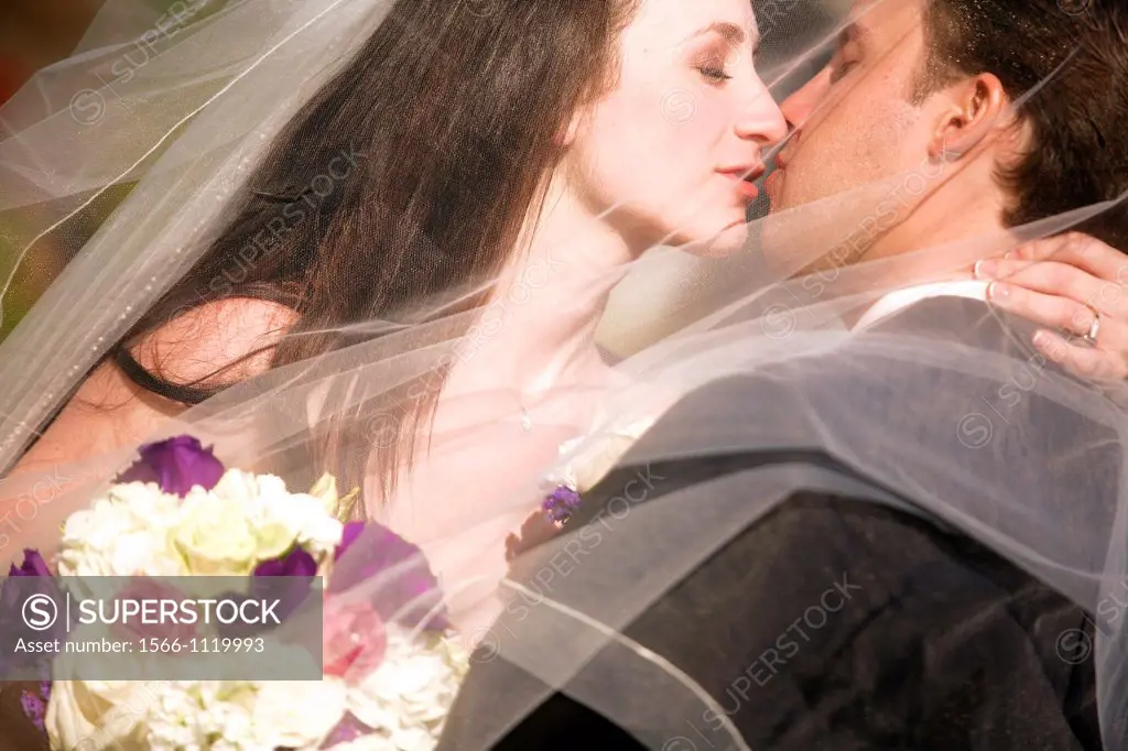 bride groom kissing embracing after wedding behind her wedding veil