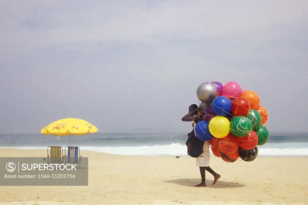 A vendor carries a net full of beach balls on his back as he walks near the shore at Ipanema beach, Rio de Janiero, Brazil.