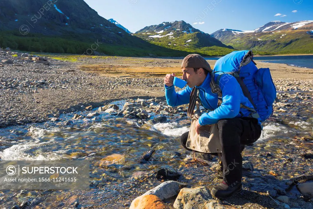 White man hiking and drinking water from a creek in stora sjöfallets national park, Gällivare, Swedish lapland.
