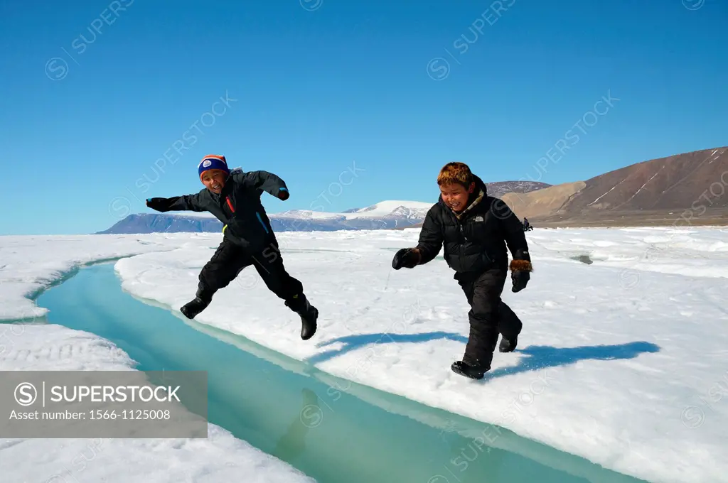 Two young Inuit boys jumping over a crack on ice floe Ellesmere island, Nanavut, Canada