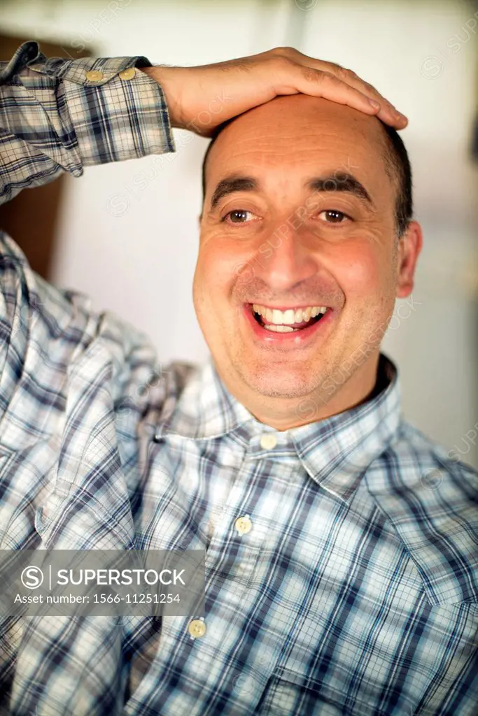 Close-up of the face of a 40-year-old Caucasian man, smiling and positive attitude, with one hand on his head and wearing plaid shirt.