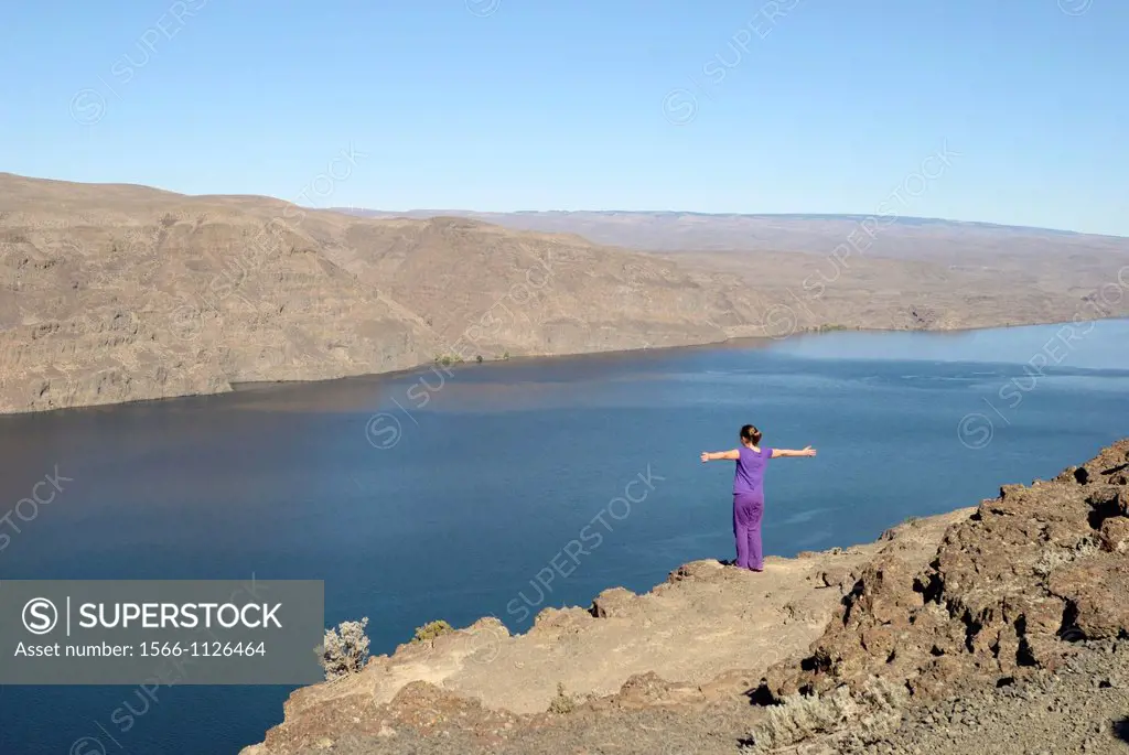 A young girl on a cliff stretching her arms near the Columbia River at a scenic outlook near Ellensburg, Washington, United States.