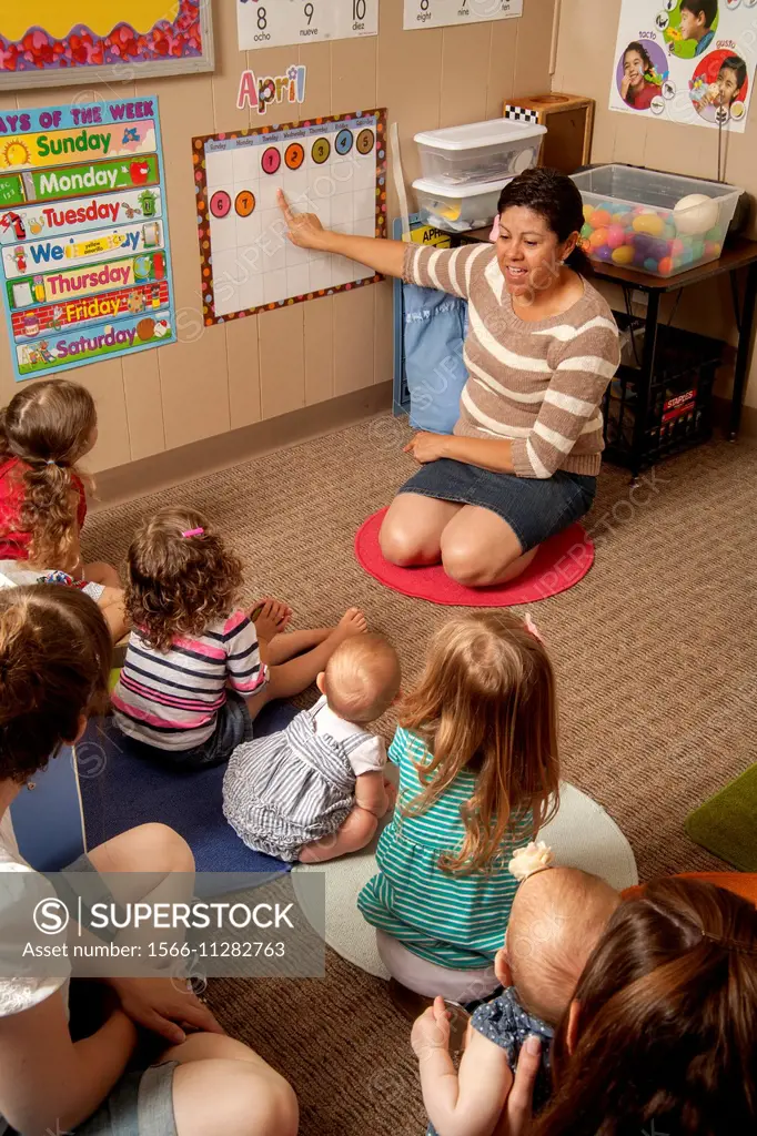 Explaining the calendar, a Hispanic teacher works with young children and their parents at a ""Learning Link"" classroom in Tustin, CA, conducting a w...