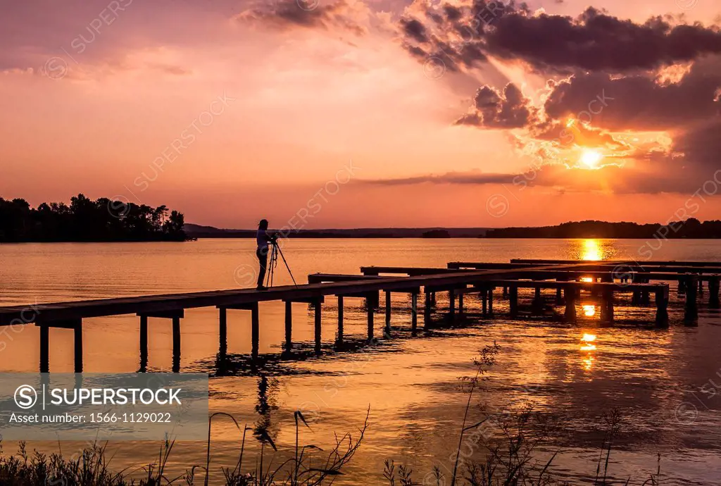 Sunset over a lake with a small boat dock and a photographer silhouetted in the foreground, Lake Guntersville State Park, Alabama, USA.