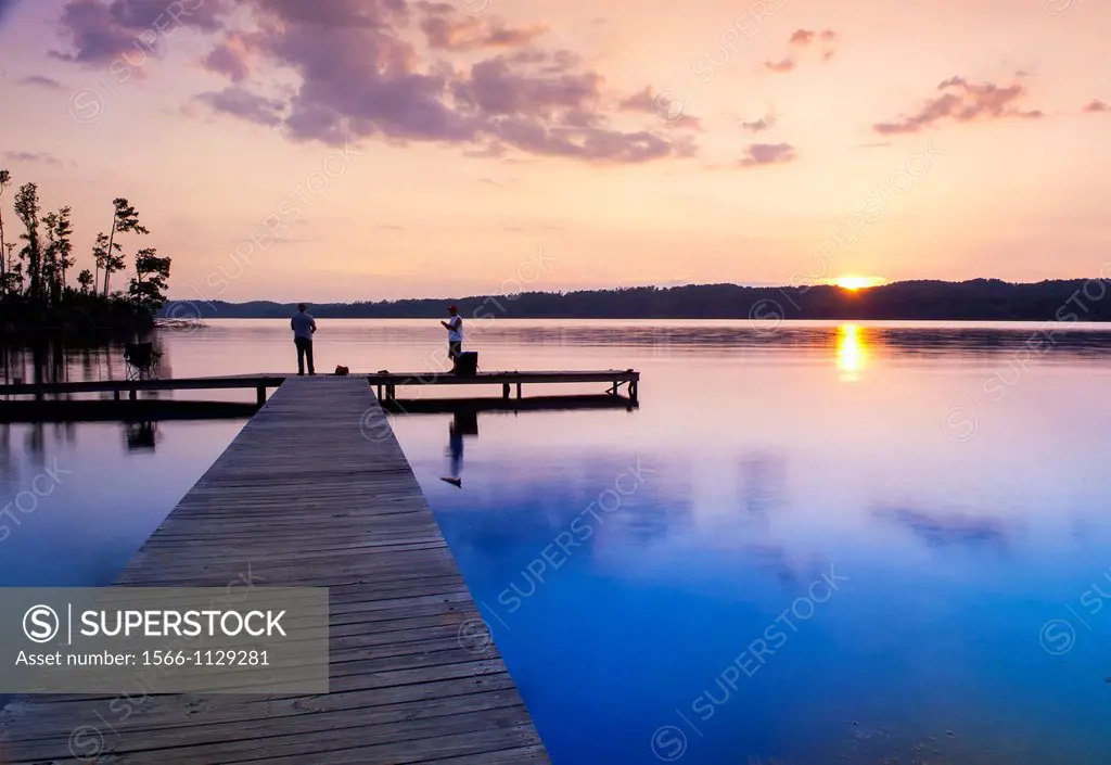 Sunset over a lake with a small boat dock and fishermen silhouetted in the foreground, Lake Guntersville State Park, Alabama, USA.