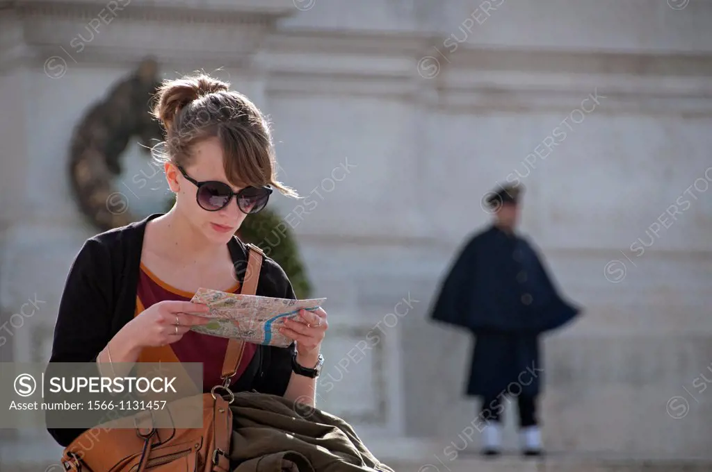 young woman studing map, Piazza Venezia, Rome, Italy, in the background National memorial of King Viktor Emanuel II, Vittoriano, honor guard at the Mo...