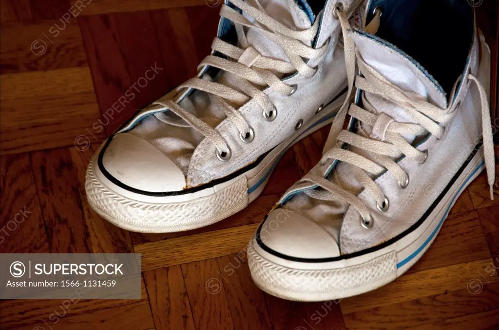 pair of white, used sneakers on the wooden floor
