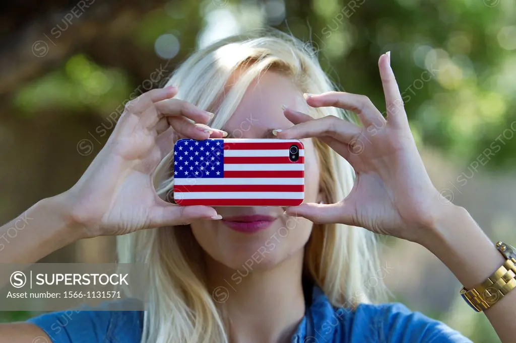 Young blonde girl taking pictures with an iPhone decorated with American flag