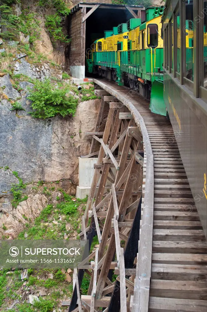 A sightseeing train crosses a precarious trestle to enter a tunnel along Alaska´s White Pass