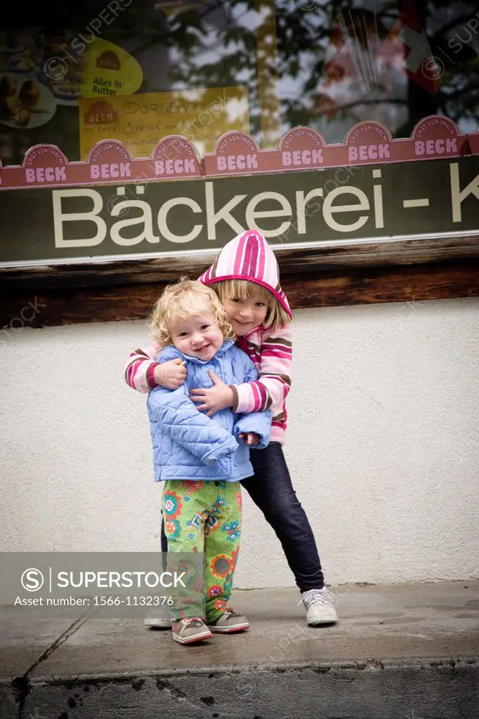 Sisters hugging and smiling at the camera in front of a backery in Mürren, Switzerland