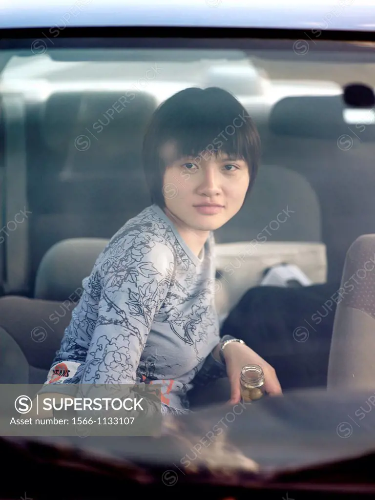 A young asian woman through a car windshield, looks at the camera
