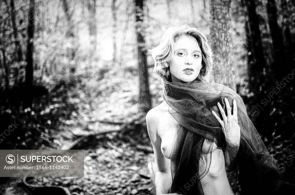 A 29 year old blond woman in a forest, partially nude, wrapped in a cloth looking at the camera