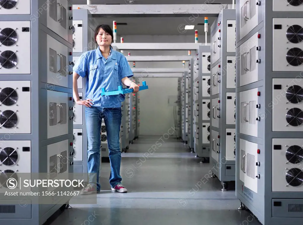 A employee of a Battery factory standing in a room of industrial-sized Li-ion battery chargers, where the batteries are brought for their intial charg...