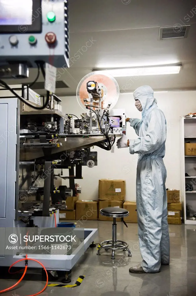 A factory worker dressed in an anti-contamination suit inspecting a machine that creates the active interior of a battery cell. Shot in a Li-ion Batte...