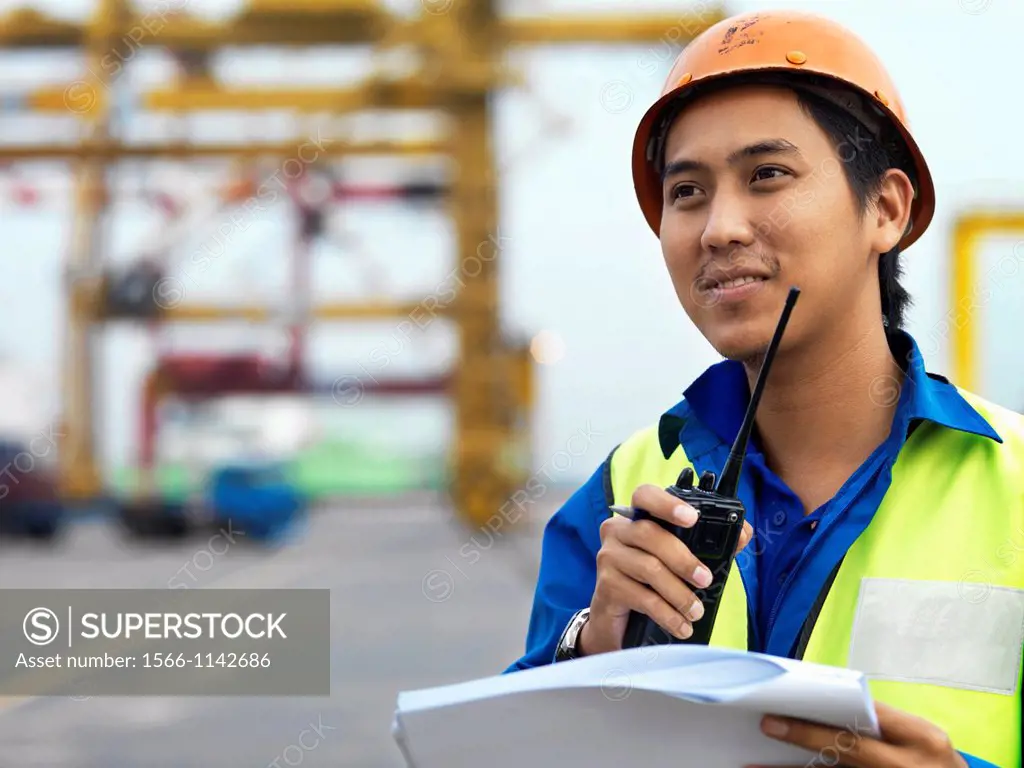 A port worker talking over and radio overseeing work at a commerical container and Palm Oil port in Johor, Malaysia