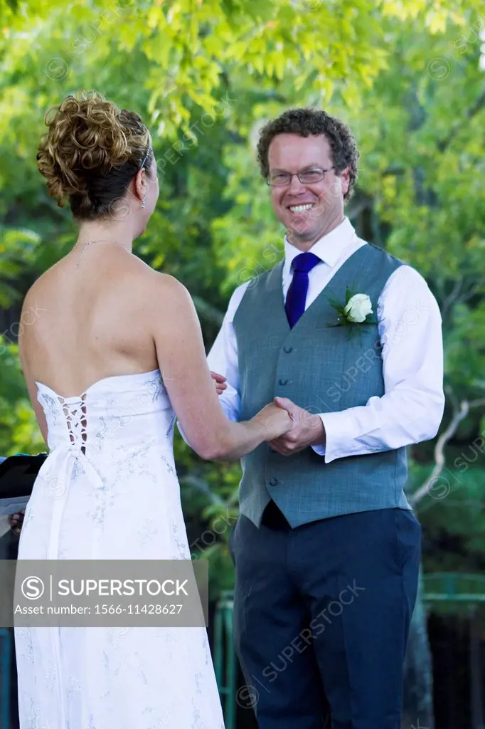 A caucasian curly hair man in his 30´s happy, with a big smile on his face, holding the brides hand. The wedding of a curly hair caucasian geek with a...