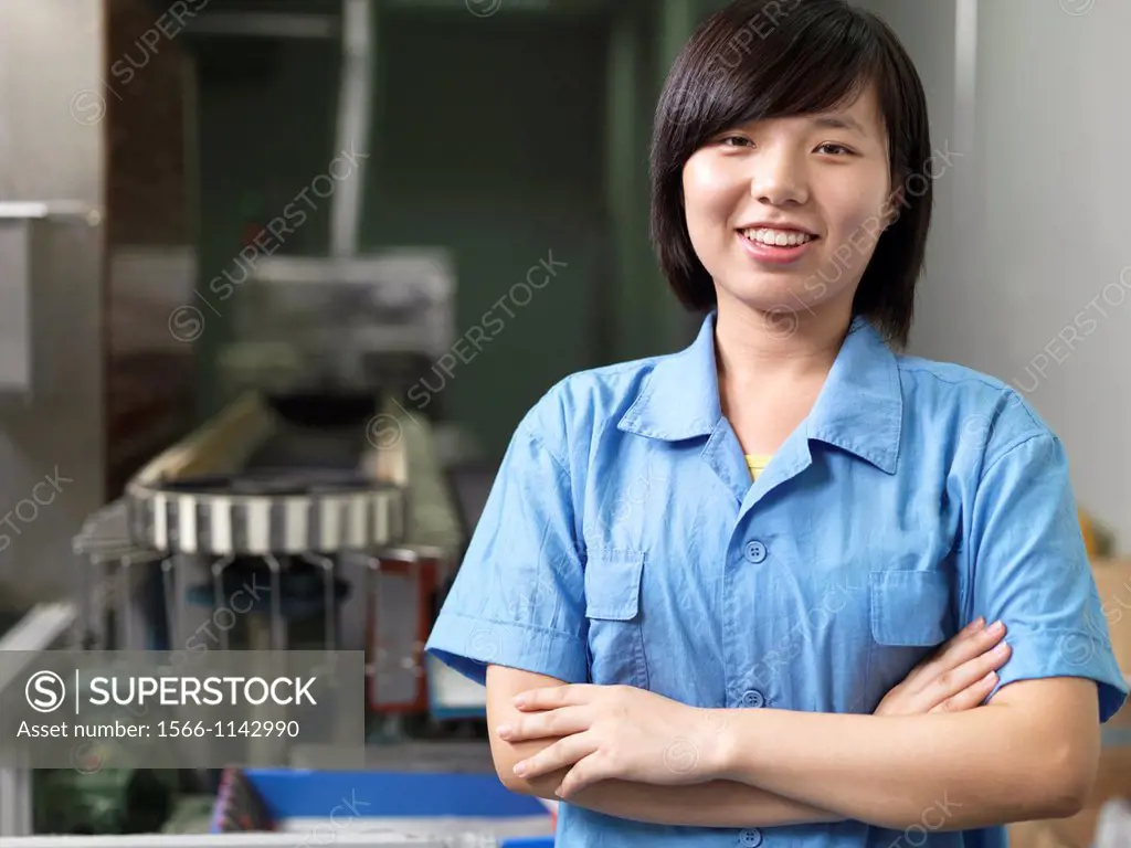A smiling factoy worker standing near industrial equipment in a Li-ion Battery Co which develops, manufactures, and markets cylindrical type rechargea...