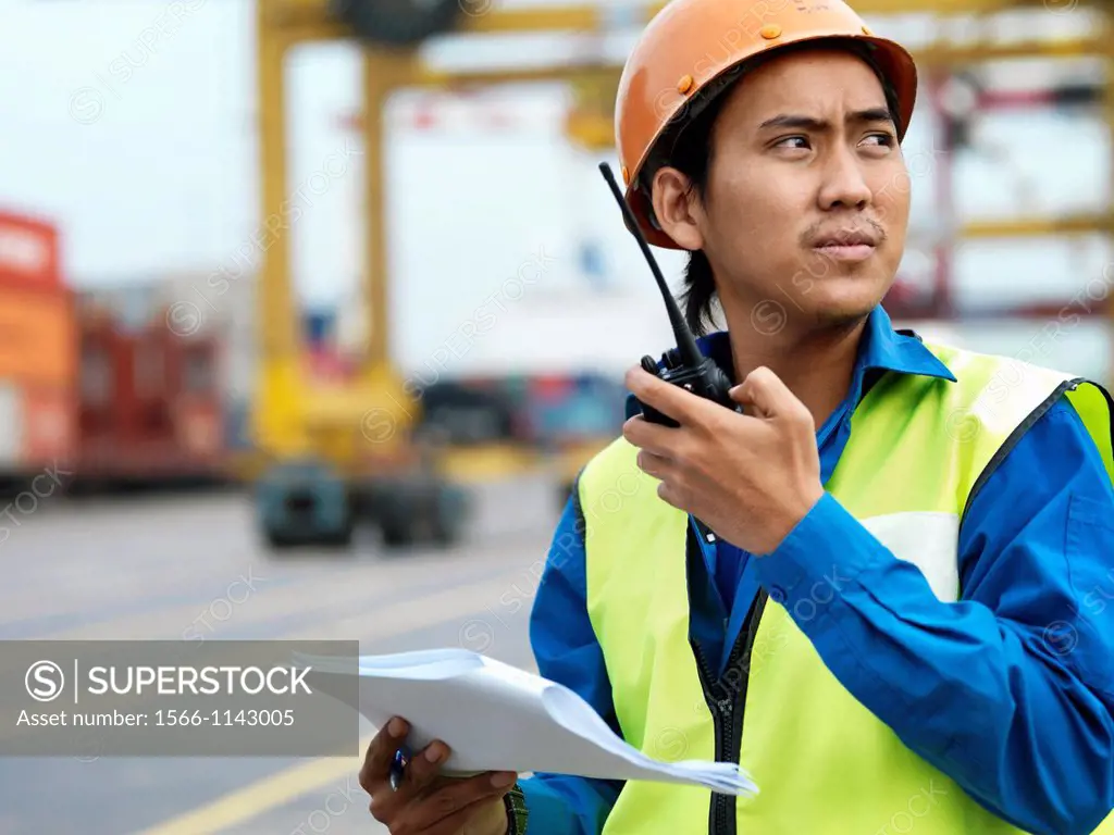 A port worker talking over and radio overseeing work at a commerical container and Palm Oil port in Johor, Malaysia