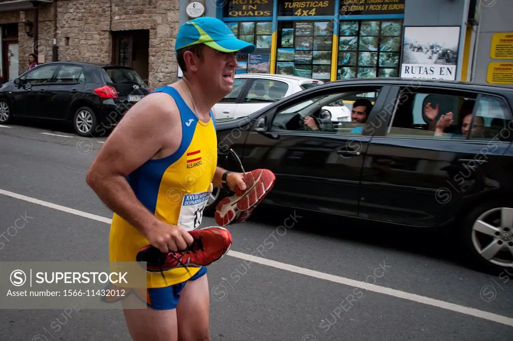 A runner reaches the finish line with shoes in hand that hurt him, while being applauded from a car. Potes, Cantabria, Spain.