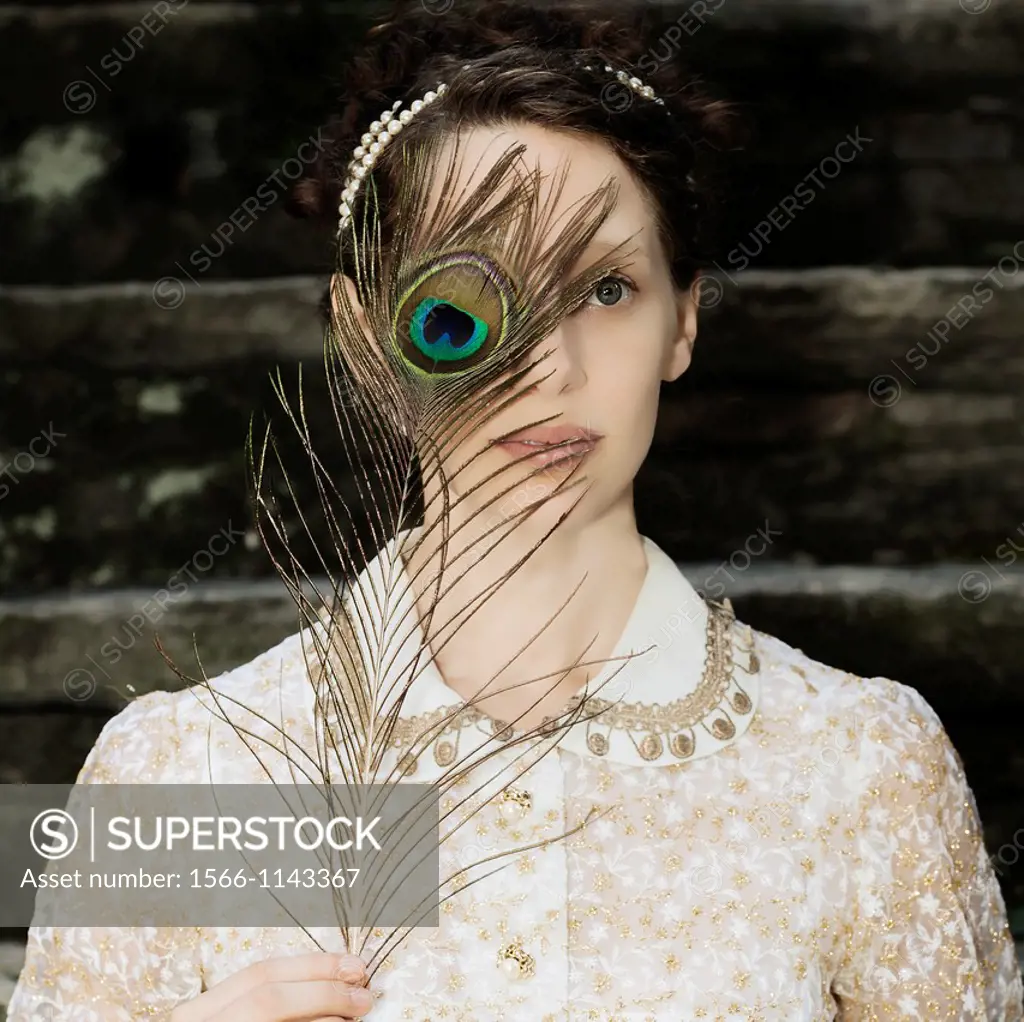 a woman with a victorian dress is holding a peacock feather in front of her eyes