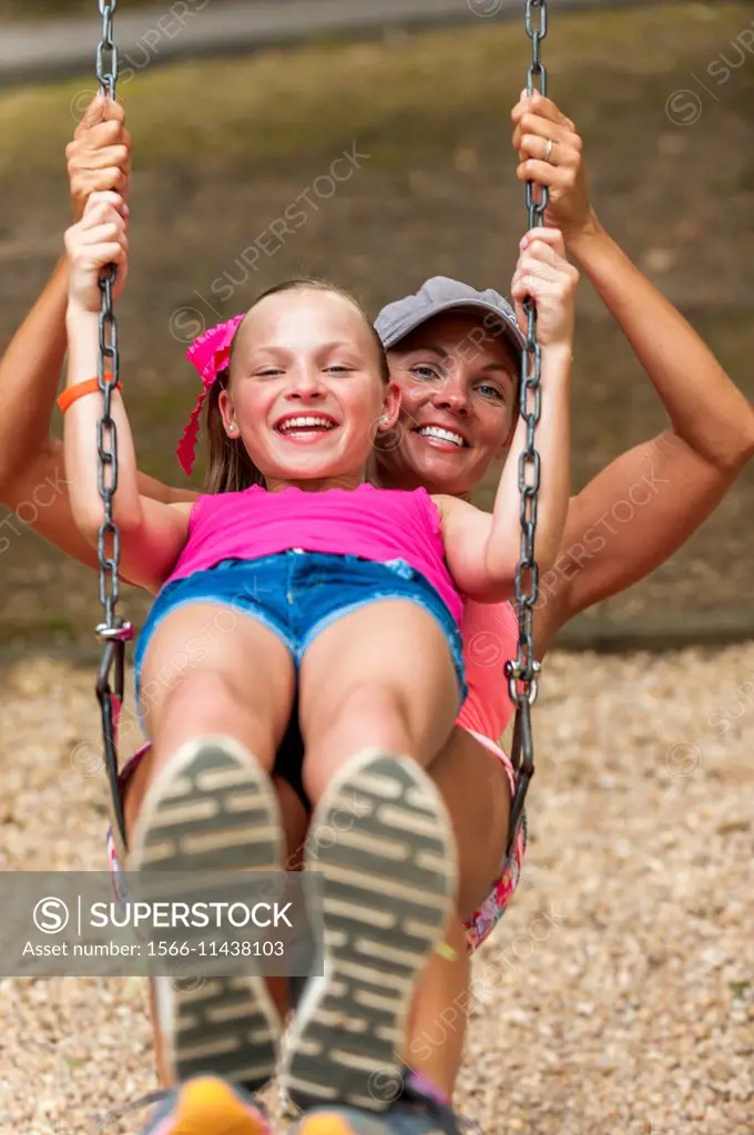 A mother and daughter share a swing at a play ground.