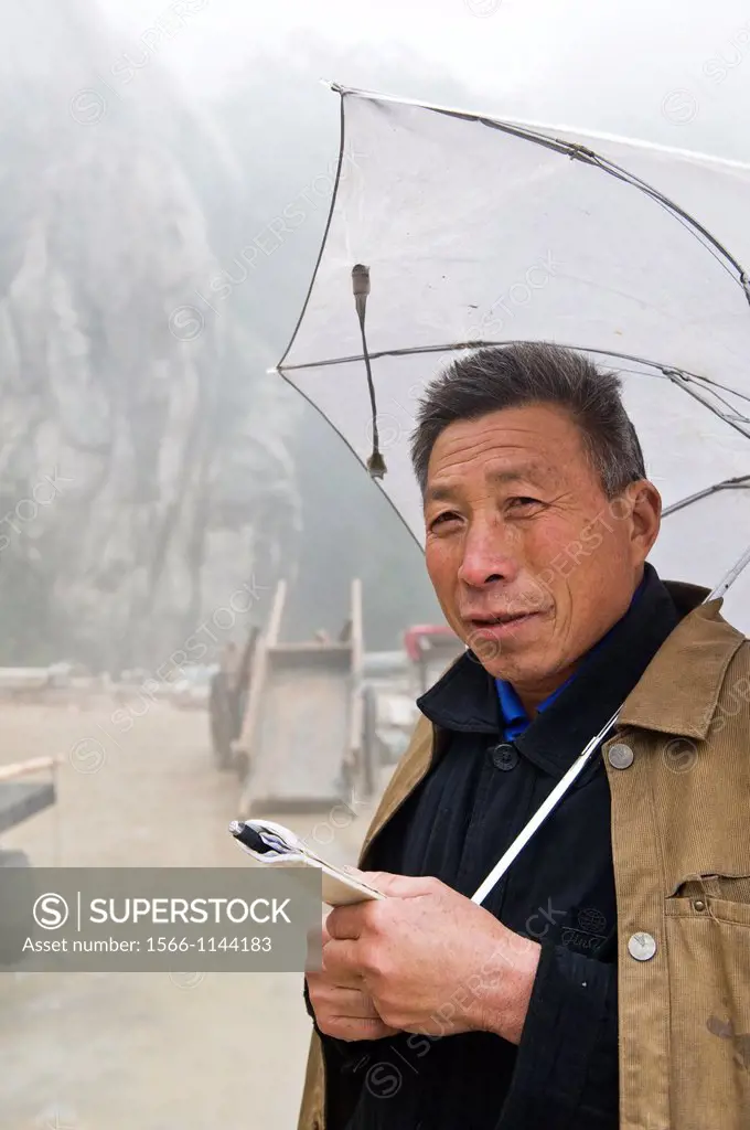 A foreman with an umbrella overseas work at the San Huang Zhai Monastery on the Song Mountain, China