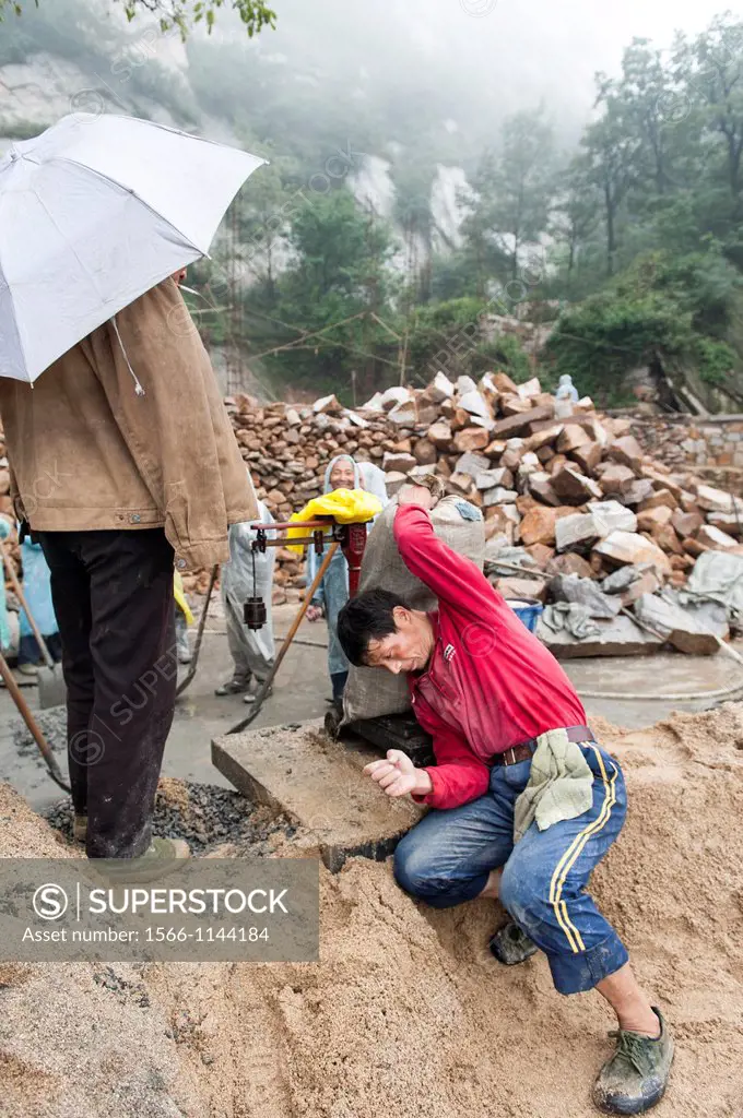 A worker struggle to put a sack of concrete on a scale at a construction site at the San Huang Zhai Monastery on the Song Mountain, China