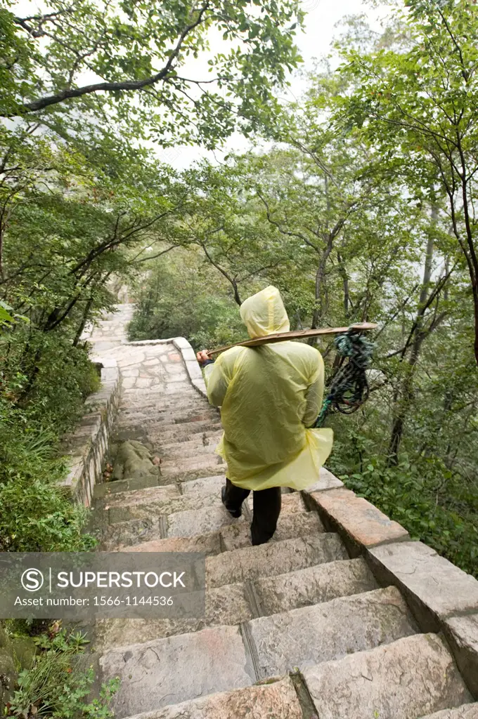 A man wearing a poncho and carrying equipment on the trail to the San Huang Zhai Monastery on the Song Mountain