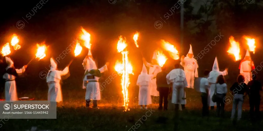KKK members holding torches while burning a cross. 1986 Klu Klux Klan event in rural Maryland USA.