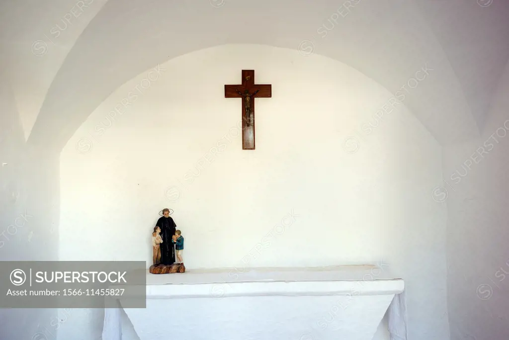 Interior of a small chapel with a crucifix on the wall and a holy figure in the altar. Menorca, Balearics, Spain, Europe