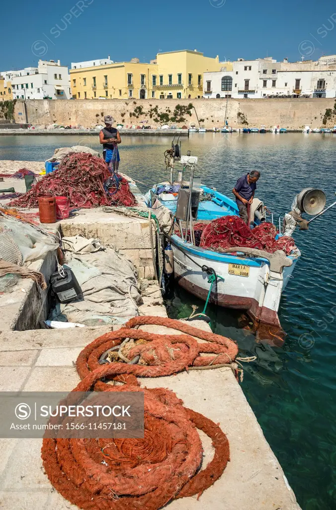 Fishermen mending fishing nets and cleaning boats at the quay in the old  town of Gallipoli, Puglia, Southern Italy. - SuperStock