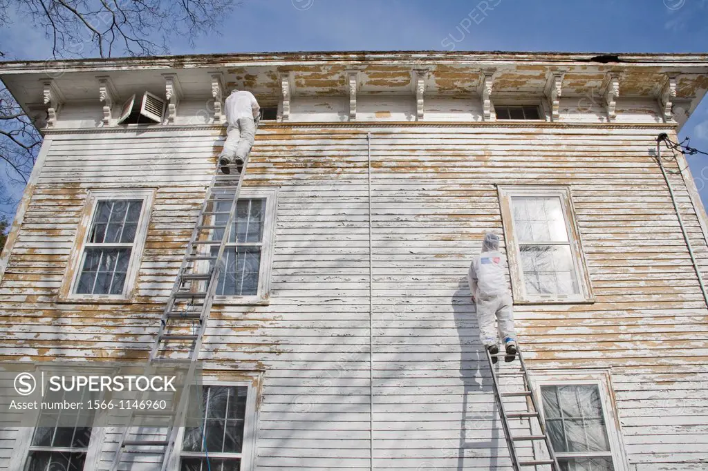 Painters, in protective clothing, scraping paint off an old house