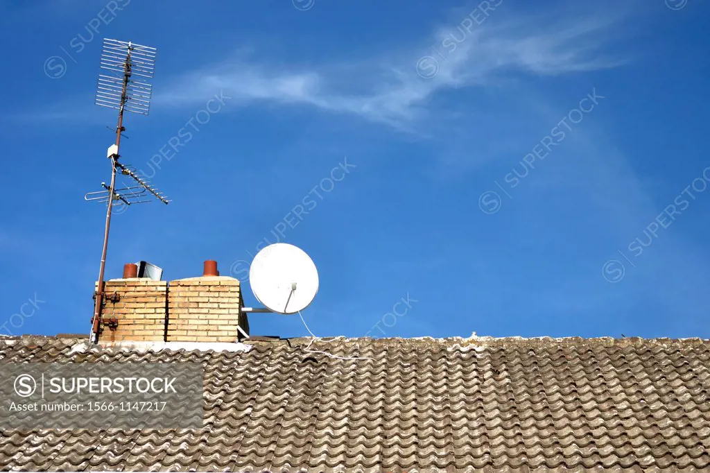 roof of an apartment building with TV antennae and satellite dish on roof by chimney