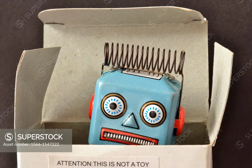 light blue wind-up robot, showing head with electrical coil peaking out of box with notice on box saying: ´Attention: This is not a toy ´