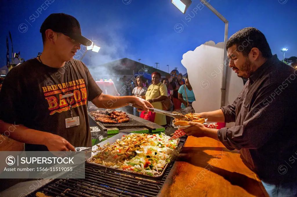 A Hispanic customer buys a grilled sausage and vegetables from a fast food vendor at the Orange County Fait in Costa Mesa, CA. Note T shirt advertisin...