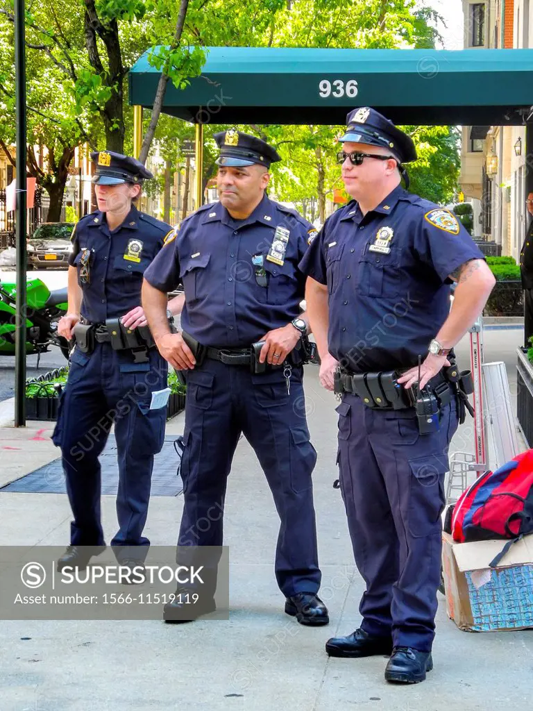 One female and two male police officers stand on a sidewalk on the Upper East Side on Manhattan, New York City.