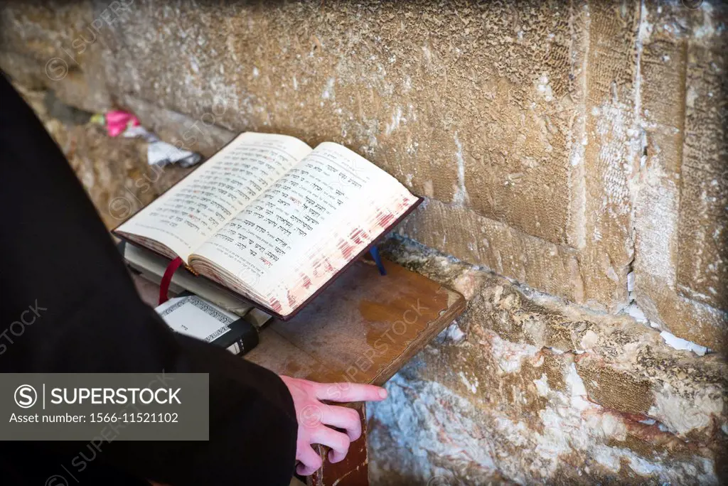 Closeup of the hand of a unrecognizable jewish man seen from behind, praying with His prayer book in the Wailing Wall synagogue in Western Wall Plaza,...