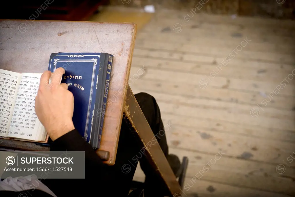 Closeup of the hand of a unrecognizable jewish man seen from behind, praying with his prayer books in the Wailing Wall synagogue in Western Wall Plaza...