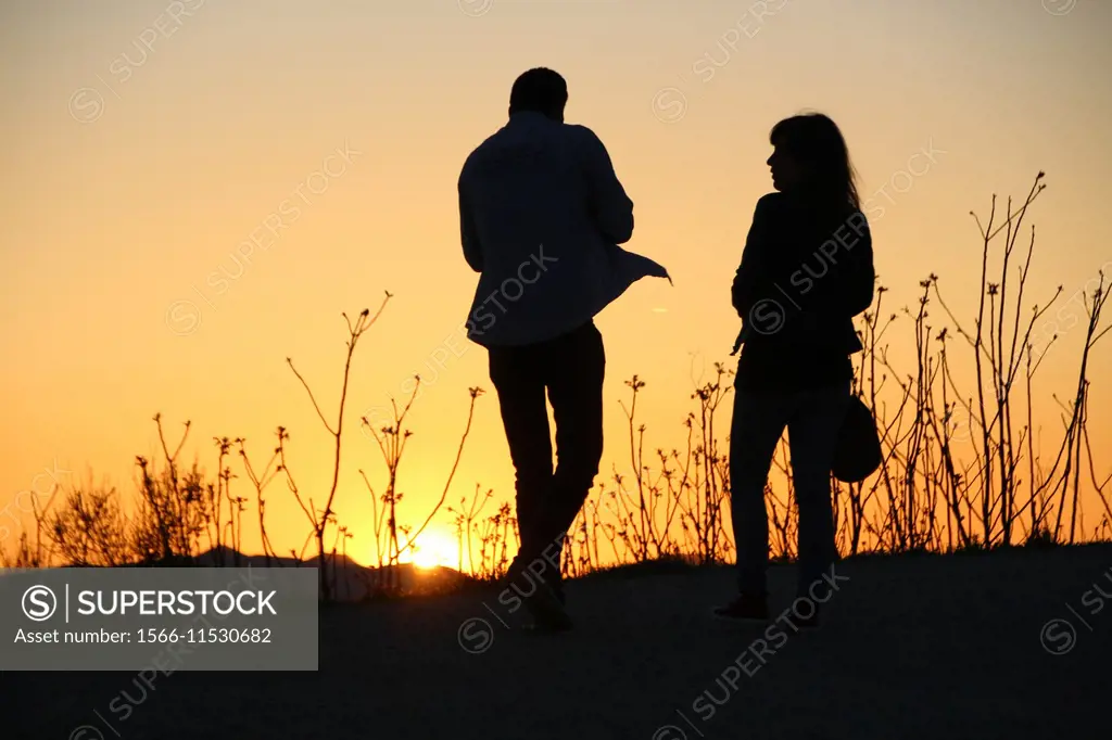 A young man and a woman walking in the sunset, Passeig de les Aigües; Collserola mountain, Barcelona, Catalonia, Spain.