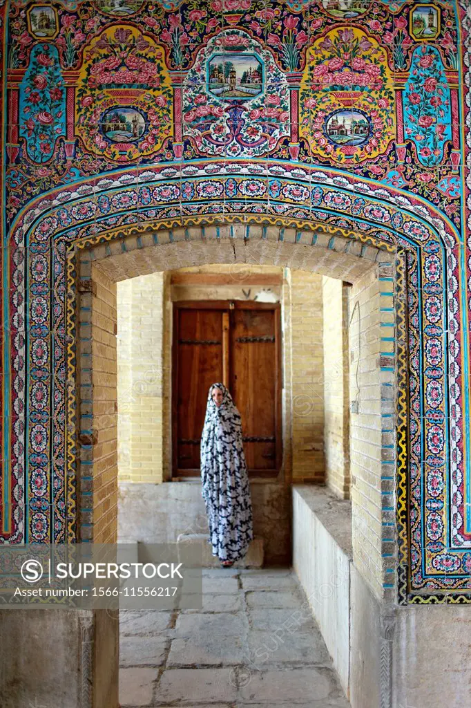 Entrance portal with wooden door and woman in the background at Nazir-al Molk Mosque (Masjed-e Nazir-al-Molk), Shiraz, Iran, Central Asia.