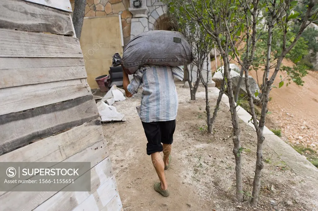 A worker carrying a heavy bag at the San Huang Zhai Monastery on the Song Mountain, China