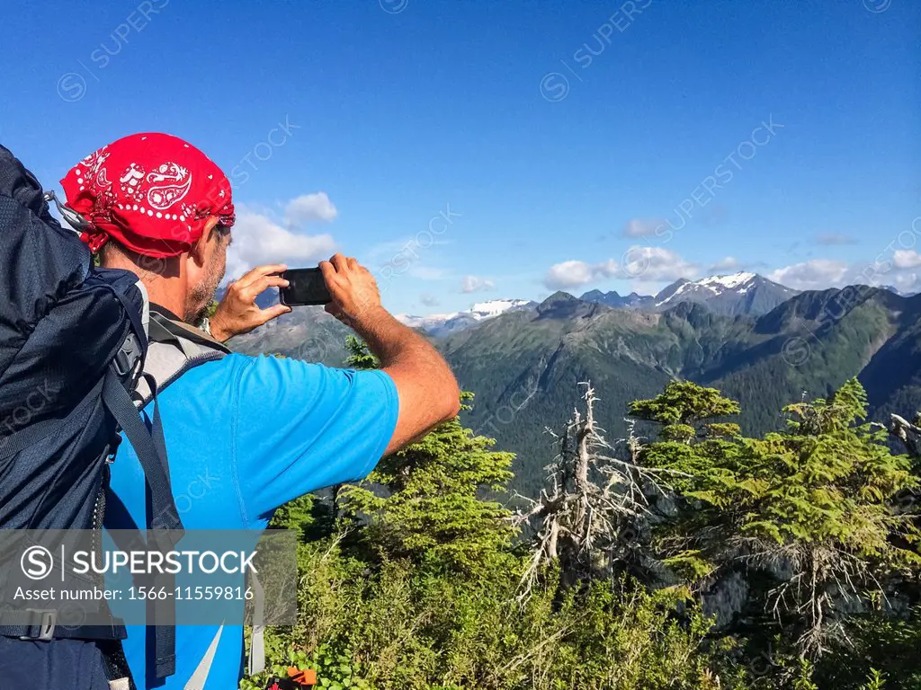 A male hiker takes and photo with his smartphone of a mountain scene.