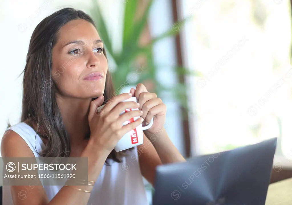 Woman working with laptop, holding mug