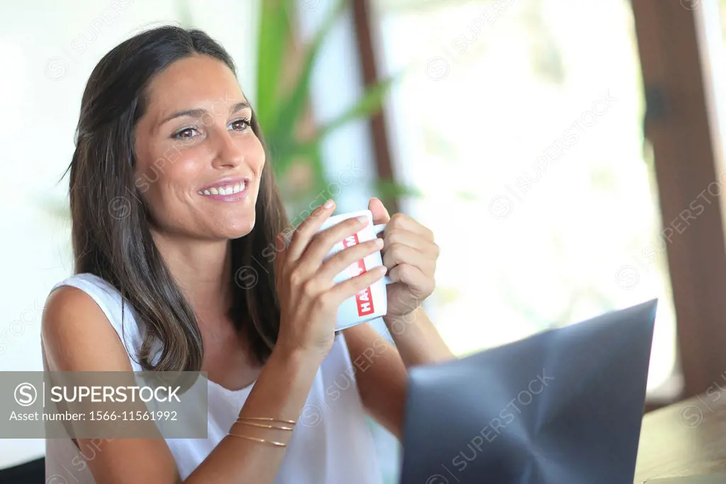 Woman working with laptop, holding mug