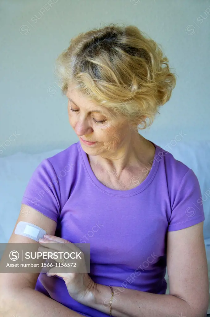 Senior woman in mauve putting a bandage on her arm