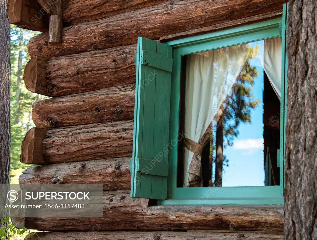 Pine trees are reflected in the window of a cabin at Tallac Historic Site