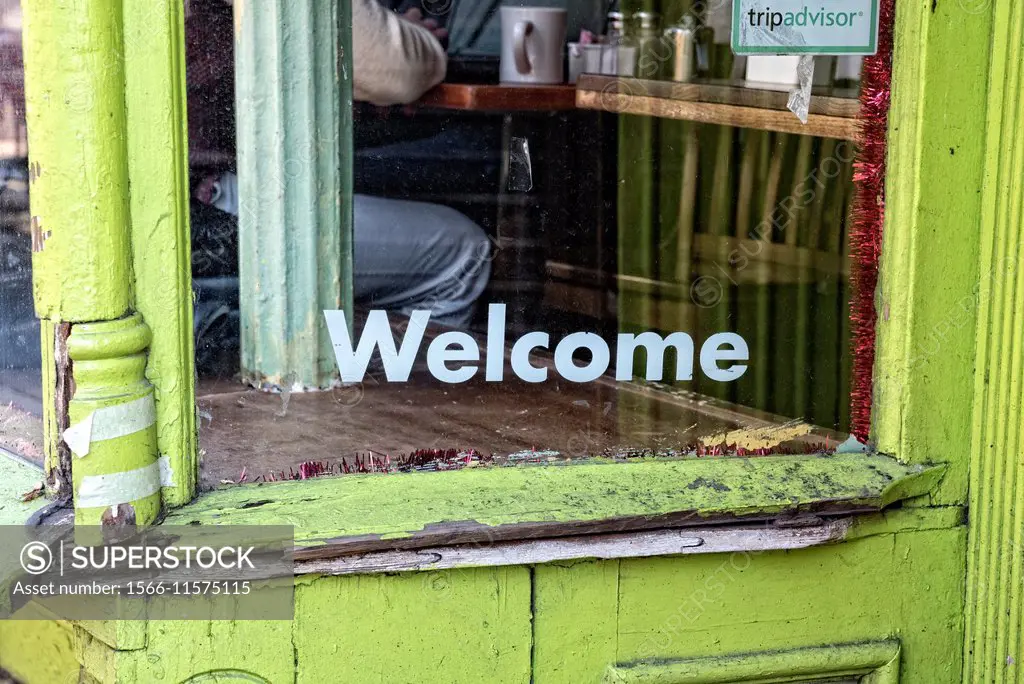Welcome Sign painted on the window of a Williamsburg, Brooklyn, NY, Coffee Shop. People seen through the glass drinking coffee.