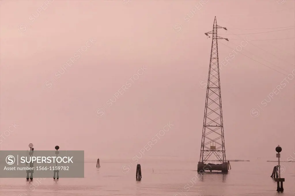 the laguna in early morning mist, with its electric pylones and ´ bricole ´ = wooden posts indicating navigable routes, Venice , Italy